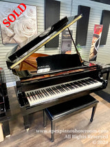 A grand piano with a glossy black finish is prominently displayed in a piano showroom with promotional material for piano series displayed in the background.