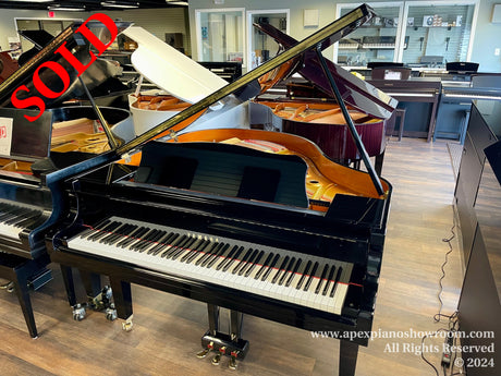 A grand piano showroom with various pianos on display, including a prominently featured black grand piano with its lid open, set amidst an array of other pianos of different styles and finishes.