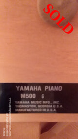 A close-up view of a Yamaha piano model label indicating YAMAHA PIANO M500 with additional text stating YAMAHA MUSIC MFG., INC. THOMASTON, GEORGIA U.S.A. MANUFACTURED IN U.S.A., affixed to the interior of a piano under the music rest.
