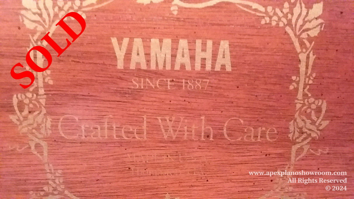 Text on a Yamaha piano soundboard reading YAMAHA SINCE 1887 Crafted With Care, with decorative floral elements etched into the wood, showcasing the brands legacy and attention to detail in piano craftsmanship.