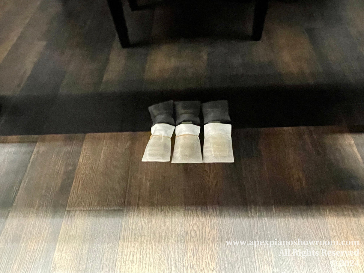 A set of four caster cups for a piano placed neatly on a wooden floor to protect the surface from potential damage due to the weight of a pianos legs.