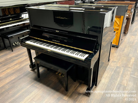 A glossy black Yamaha upright piano prominently displayed in a piano showroom with various other pianos in the background, reflecting the well-lit environment on its polished surface.