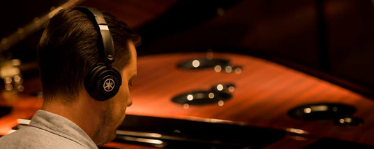 Man wearing headphones tuning a grand piano, focusing on the interior strings and hammers.