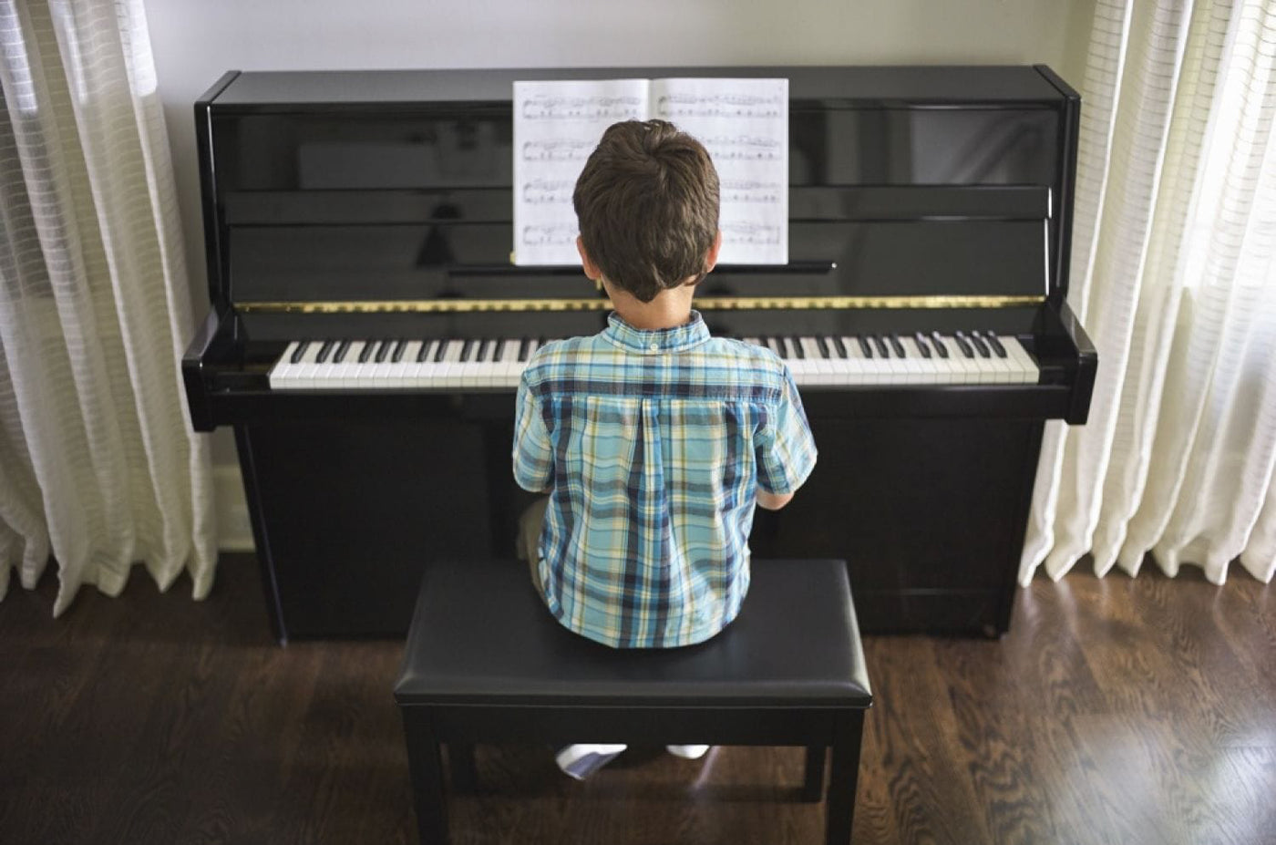 Young student sitting at an upright piano, ready to play a piece of music from the sheet music on the stand.