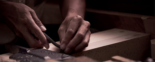 Close-up of a piano craftsman's hands meticulously filing a wooden component of a piano.