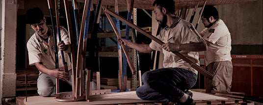 Craftsmen working on assembling a wooden piano frame in a workshop.