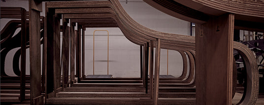 Layered wooden piano rims in a manufacturing workshop, showcasing the curved structures that form the body of grand pianos.