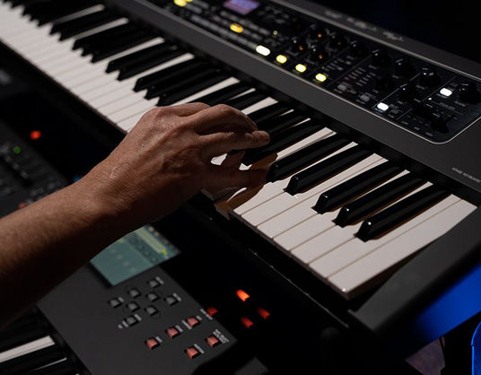 A musician's hand playing a chord on a modern electronic keyboard with LED lights and control buttons visible.