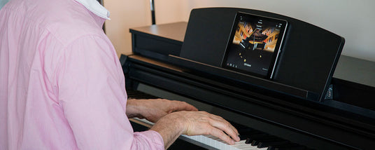 Person in a pink shirt playing a digital piano with a display showing sheet music.