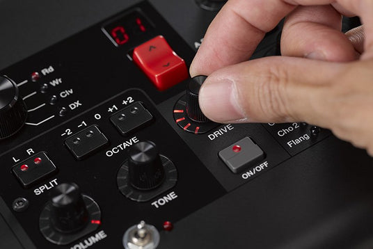 Close-up of a musician's hand adjusting the DRIVE knob on an electronic keyboard or digital piano control panel with various function buttons including OCTAVE and TONE settings.