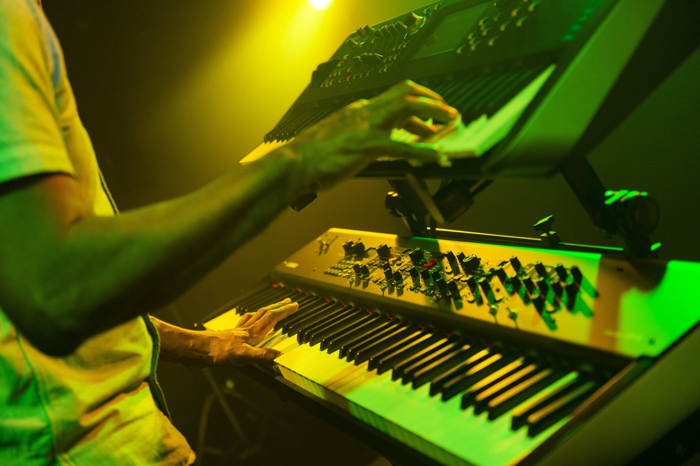 Pianist performing on an electronic keyboard with green stage lighting.