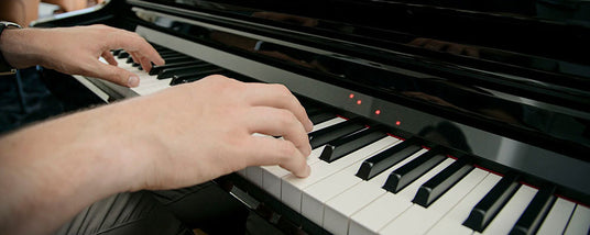 Person playing a piano, focusing on their hands pressing keys with a shallow depth of field.