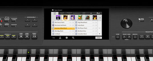 Electronic keyboard close-up showing a digital display with style select options for different rock genres and programmable buttons, with a portion of the keyboard keys visible.
