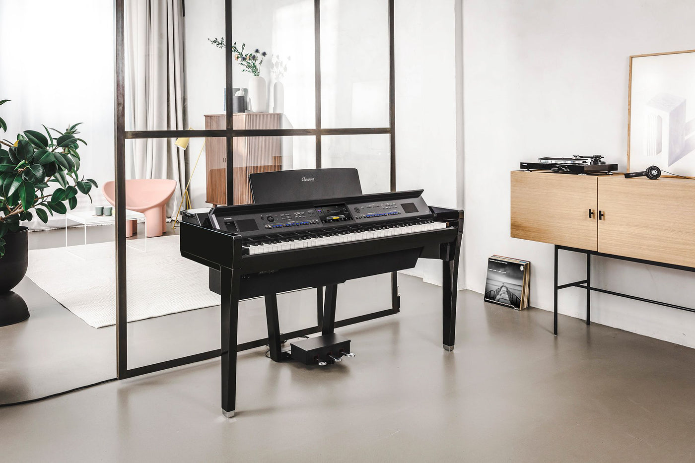 A modern digital piano with a sleek black design, sitting in a stylish living room with minimalist decor, next to a wooden sideboard with a vintage turntable on top.