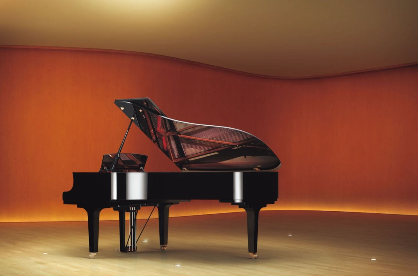A grand piano with an open lid prominently displayed in a room with warm lighting and a curved wooden wall, exemplifying elegant design and craftsmanship in piano manufacturing.