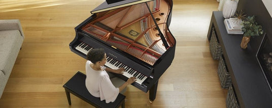 Aerial view of a woman playing a grand piano in a well-lit room with hardwood floors, embodying the artistry and elegance of piano performance.