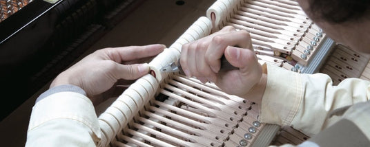 A piano technician's hands using tools to regulate the action mechanism inside a grand piano.