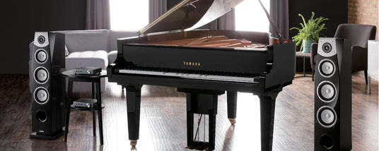 A Yamaha grand piano in a modern living room with high-end speakers on either side.