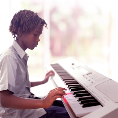 Young musician practicing on a digital piano beside a window with natural light.
