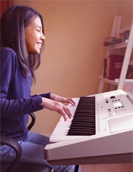 Young girl happily playing a white electronic keyboard in a home setting.