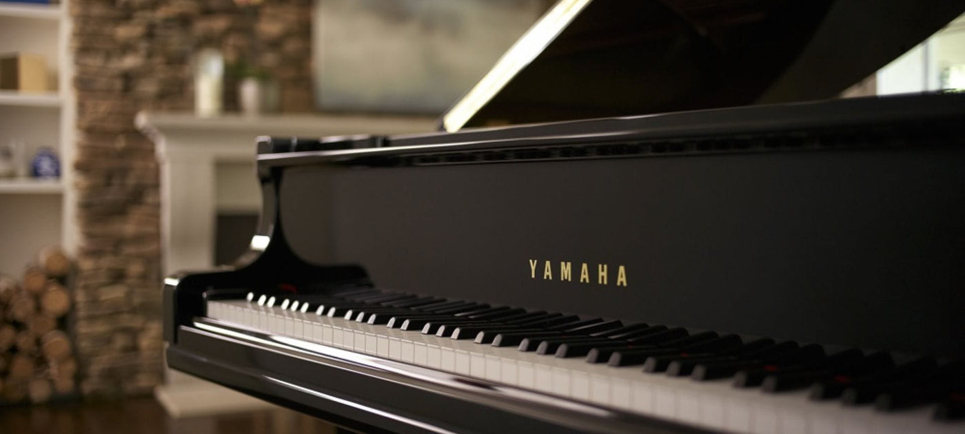 Side view of a black Yamaha grand piano with the lid open, placed in a cozy room with a fireplace and shelving in the background.