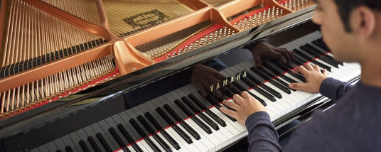 Person playing on a Yamaha grand piano, focusing on the hands and keyboard with internal strings and hammers visible.