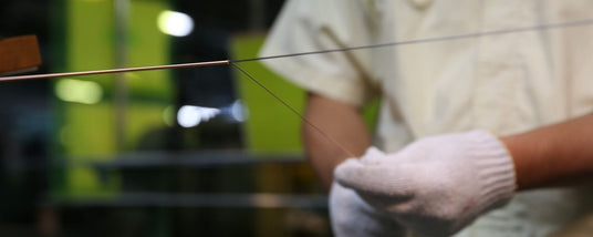 Worker in a piano string manufacturing facility inspecting the tension and quality of newly produced piano wire.