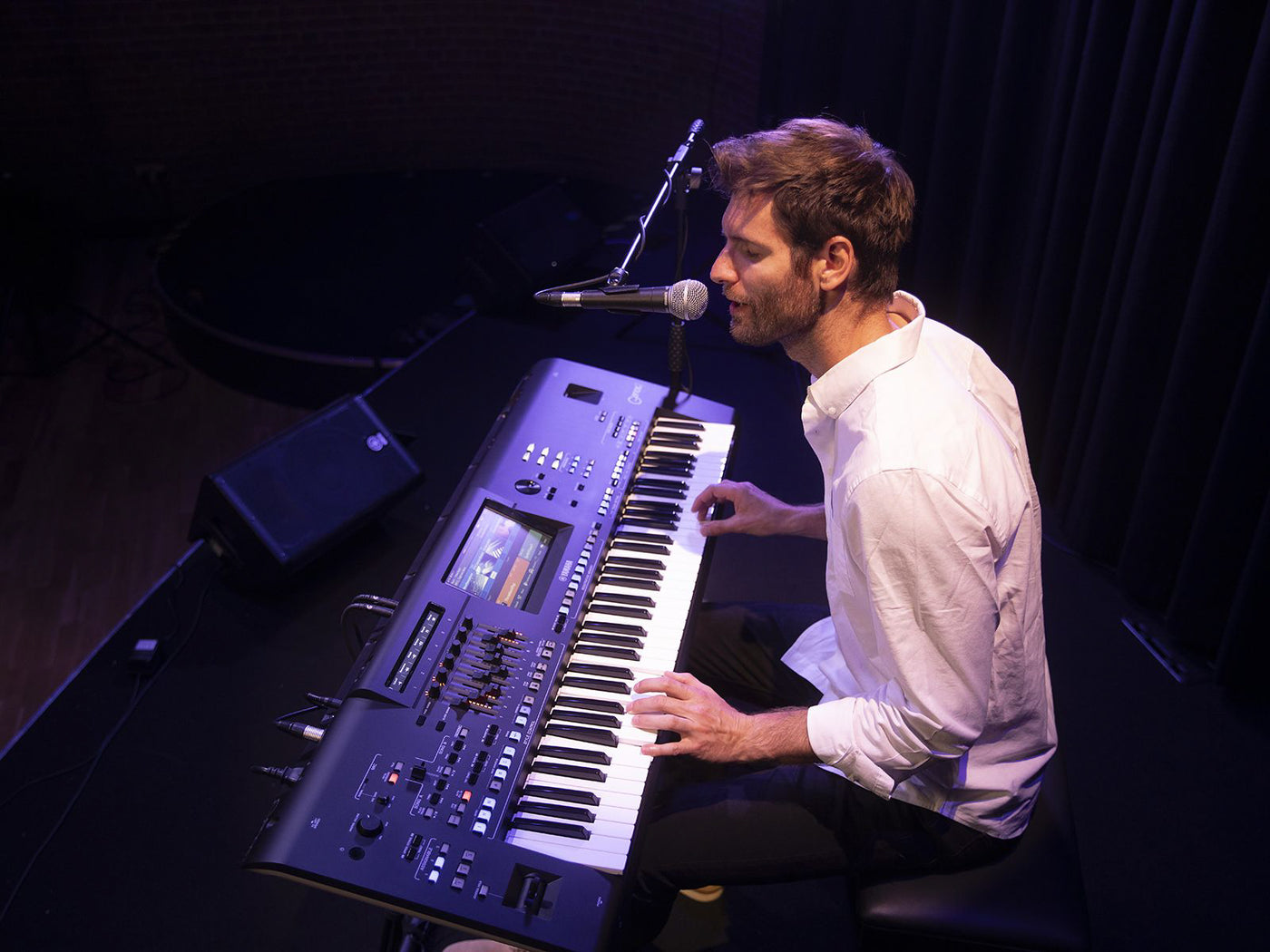 Male musician playing a digital stage piano during a live performance with microphone setup.
