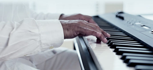 Person in white clothing playing a black digital piano, emphasizing the performer's hand movement on the keys.
