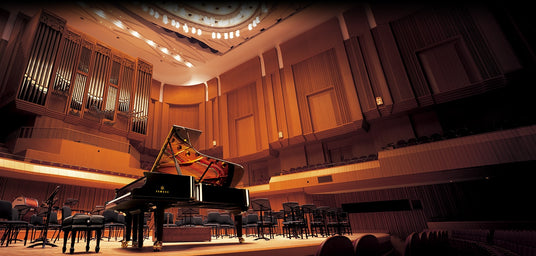 Grand piano on stage in an elegant concert hall, with seating and pipe organ in the background, illustrating a high-end performance venue for piano concerts.