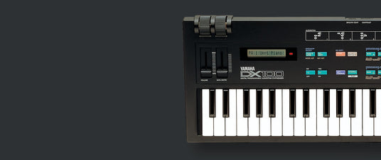Yamaha DX100 digital programmable algorithm synthesizer with labeled buttons and sliders on a dark background.