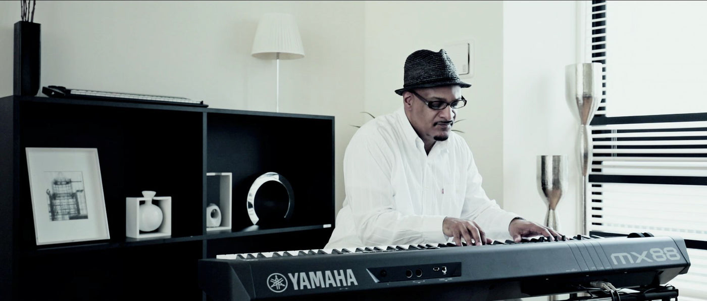 A musician playing a Yamaha MX88 keyboard in a modernly decorated room.