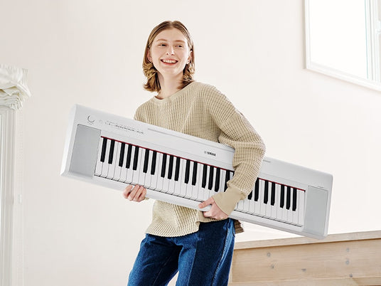 A happy individual holding a portable digital piano with enthusiasm, showcasing the instrument's lightweight and mobile design for musicians on the go.