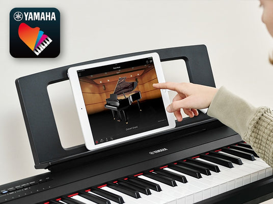 Person using a tablet with an augmented reality application to visualize a grand piano above a keyboard, with a Yamaha logo in the top left corner.