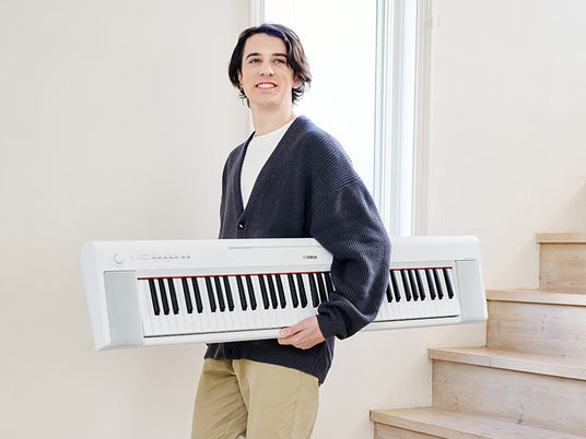 Smiling person holding a portable digital piano on the stairs in a bright, indoor setting.