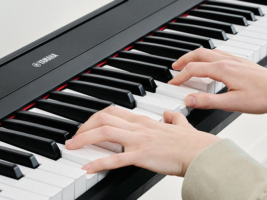 Close-up of a person's hands playing a Yamaha digital piano, focusing on the black and white keys.