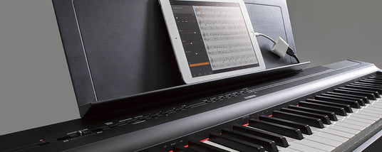 Close-up view of a digital piano with sheet music displayed on a tablet, music stand, white and black keys, and control buttons with red backlights.