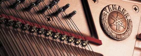 Close-up view of the interior of a Yamaha grand piano showing strings, tuning pins, and the gold Yamaha emblem.