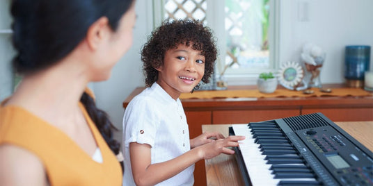 Young child happily playing on a digital piano with a female adult looking on, showcasing an early music education scene.