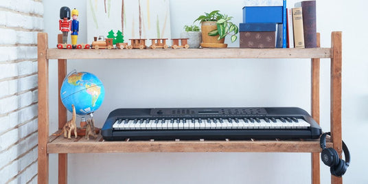 Electronic keyboard on a wooden stand with headphones, surrounded by decorative items and books, suggesting a cozy home practice set-up for piano enthusiasts.