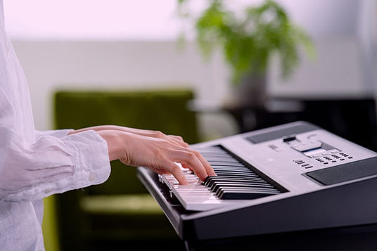 Person in a white shirt playing an electronic keyboard with a modern interior background.