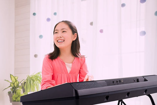 Young girl smiling and enjoying playing a digital piano in a bright room with decorative elements in the background.
