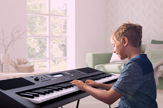 Young boy practicing on a digital keyboard in a home setting with natural light coming from a window.