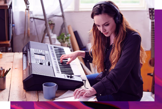 Woman wearing headphones playing a digital piano in a home studio setting.