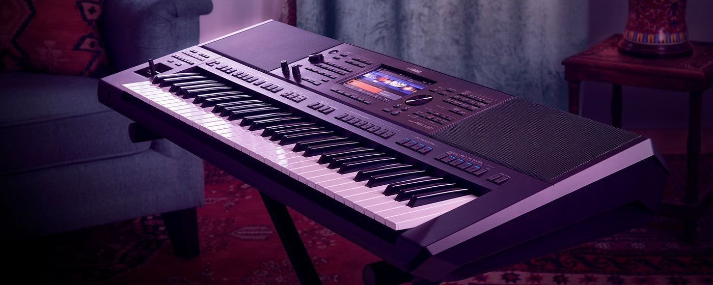 An electronic keyboard with illuminated keys and a display screen, placed on a stand in a dimly lit room with decorative elements.