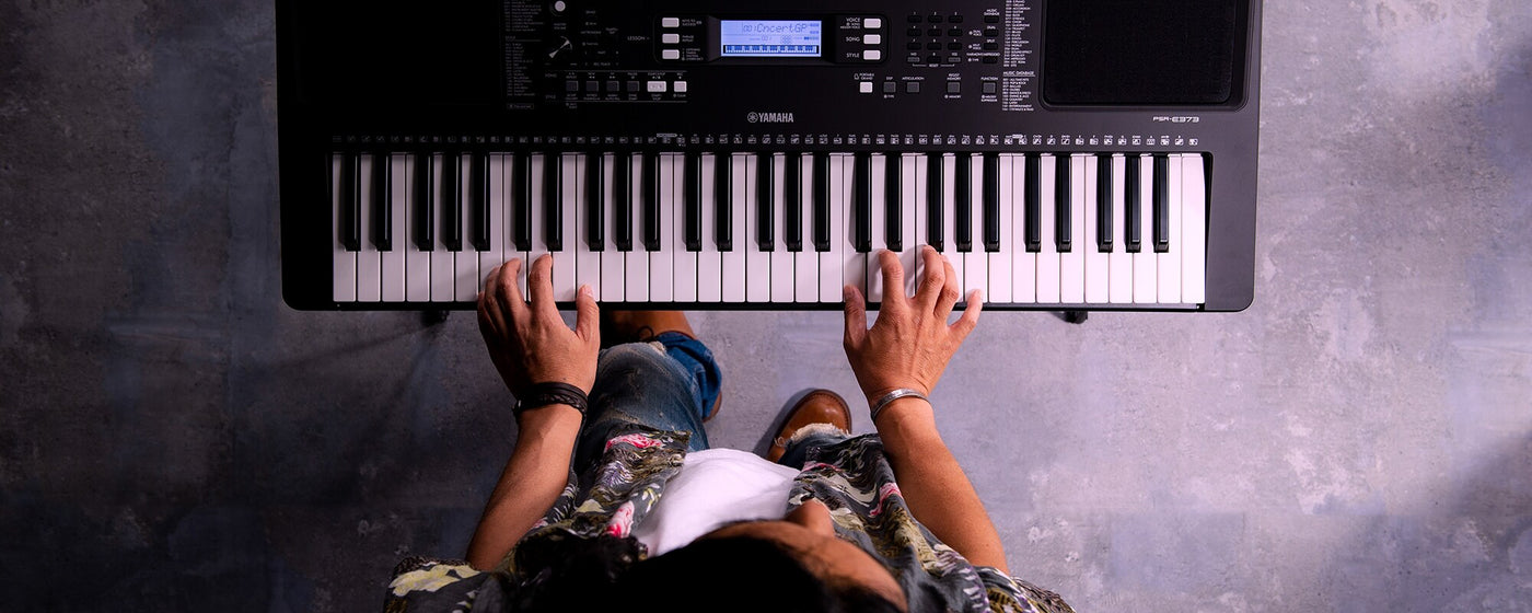 Person playing on a Yamaha electronic keyboard with view from above showing hands on keys and display screen.