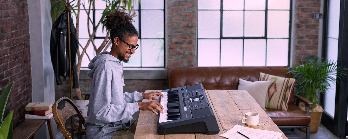A musician enjoying playing a modern electric keyboard in a cozy urban apartment setting with exposed brick walls and large windows.