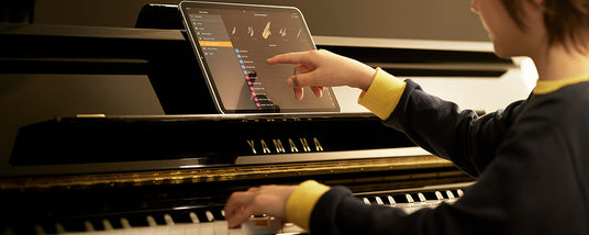A person selecting a music score on a digital device placed on the music rest of a Yamaha grand piano.