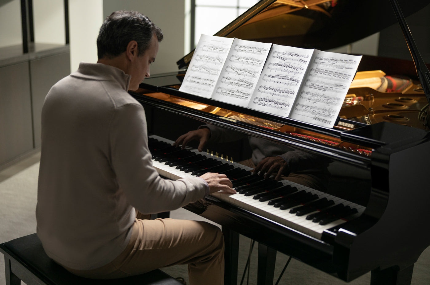 Pianist practicing on a black grand piano with sheet music open on the music rest.
