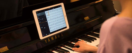 A pianist using a digital sheet music app on a tablet placed on the music stand of a Yamaha grand piano.